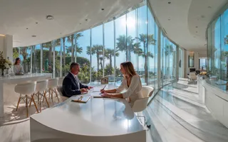 Professional notary and realtor meeting with a client in a bright modern office overlooking palm trees and the coast, representing a white-glove real estate closing experience in Tampa Bay